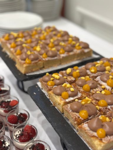 Dessert Süßer Blechkuchen mit Schokoladenglasur und goldenen Früchten, daneben kleine Dessertgläser.