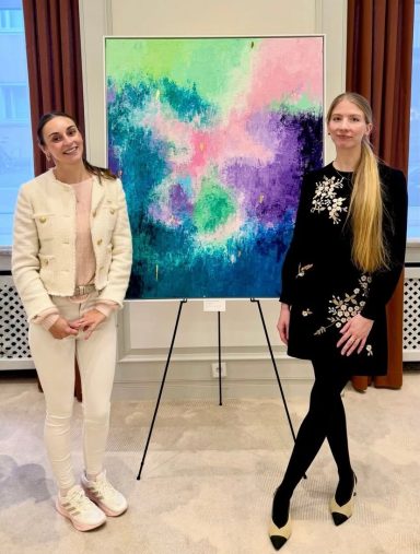 Organisatorin Miriam Guba mit Künstlerin Carola Fleischhauer vor einem ihrer Werke Zwei Frauen stehen neben einem farbenfrohen Gemälde in einem hellen Raum.